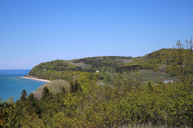 A scenic overlook showing hills and valleys with farms in them. There are patches of forest and a large lake on the left.
