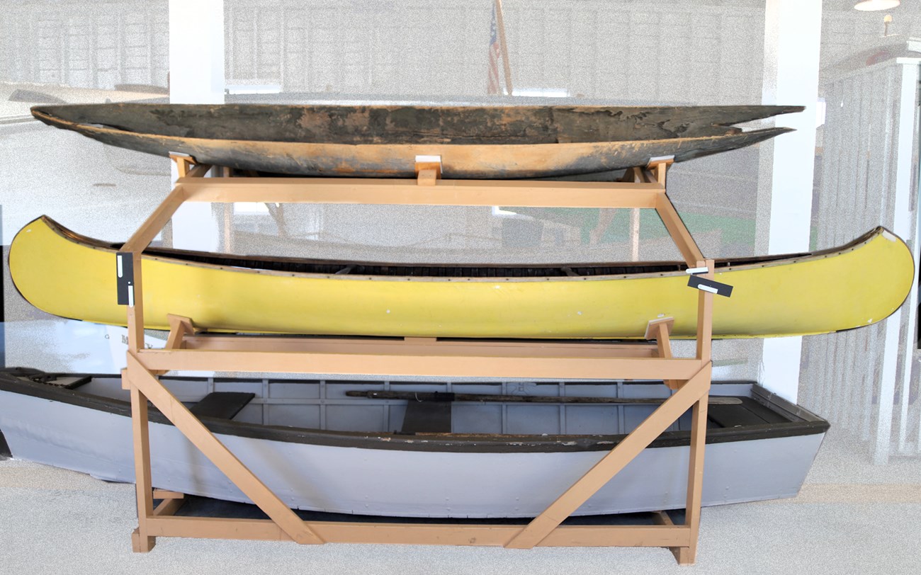 A rack holds three boats: a dugout canoe, a yellow canoe, and rowboat
