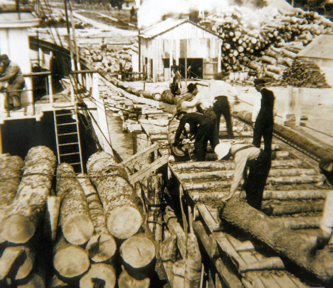 Historic photo of men loading logs alongside a large wooden dock