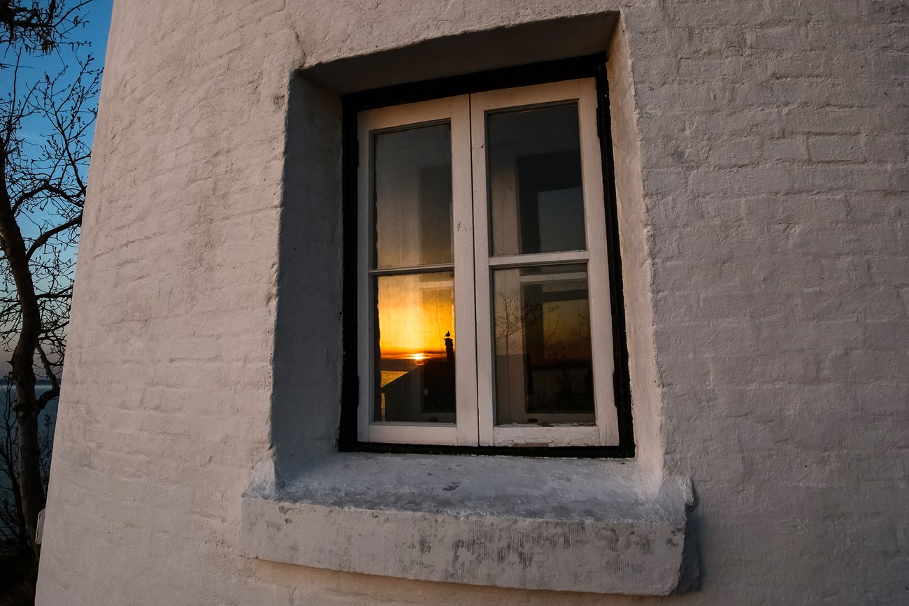 Sunset is captured in the lighthouse window reflection