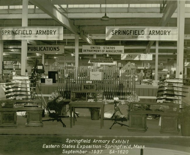 A display of firearms made at Springfield Armory at an exposition with other displays in the background.