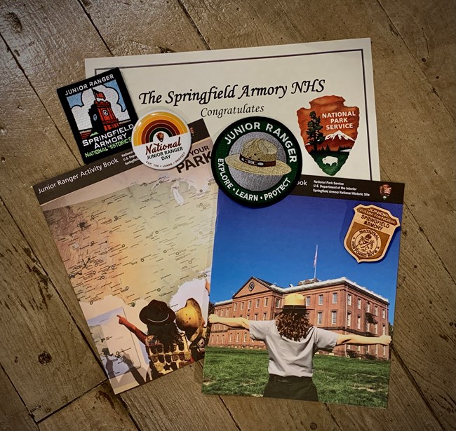 Two Junior Ranger Booklets, a certificate and a couple of park patches lay against a wood backdrop.