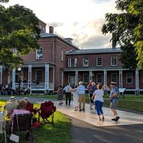 Bad News Jazz and Blues Orchestra Couples dancing with an orchestra visible in the distance performing in front of a brick mansion