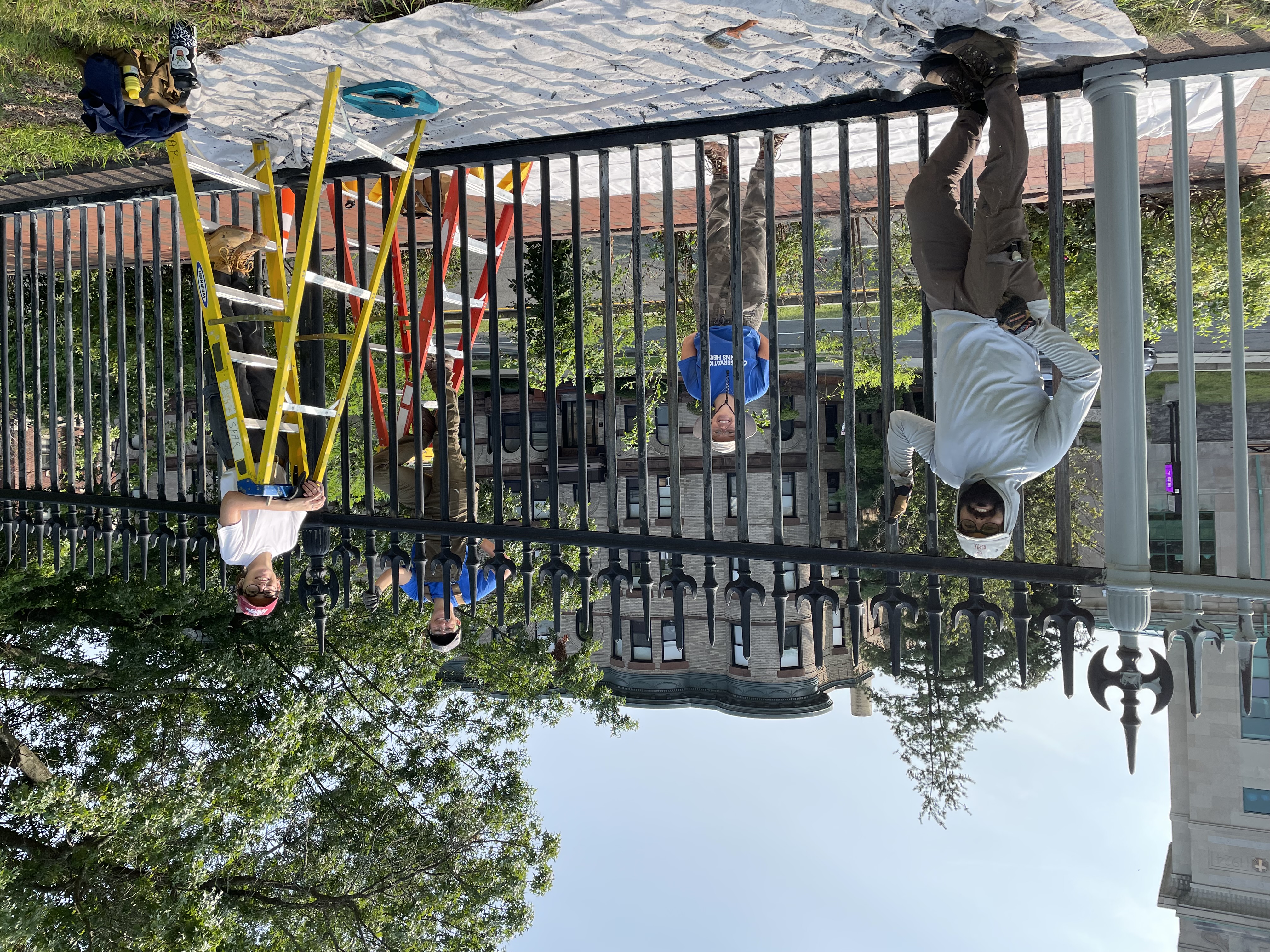 Four people standing along an iron fence. Two people are standing on ladders.