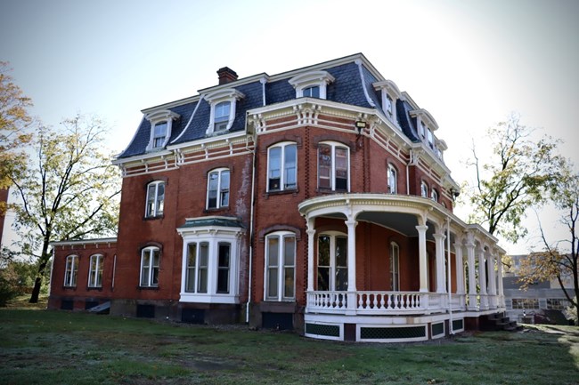 A multistory red brick house with a covered porch and an addition in the rear.