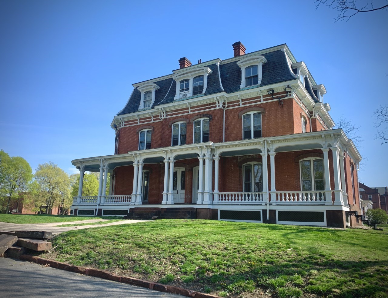 A multistory red brick building with an angled roof and a covered porch. There are multiple windows.