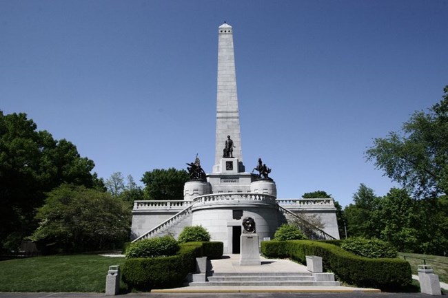 A tall, stone obelisk with a stone structure underneath and multiple metal statues.