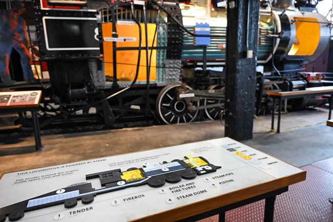 A tactile graphic of the cutaway steam engine in the foreground, with the cutaway in the background.