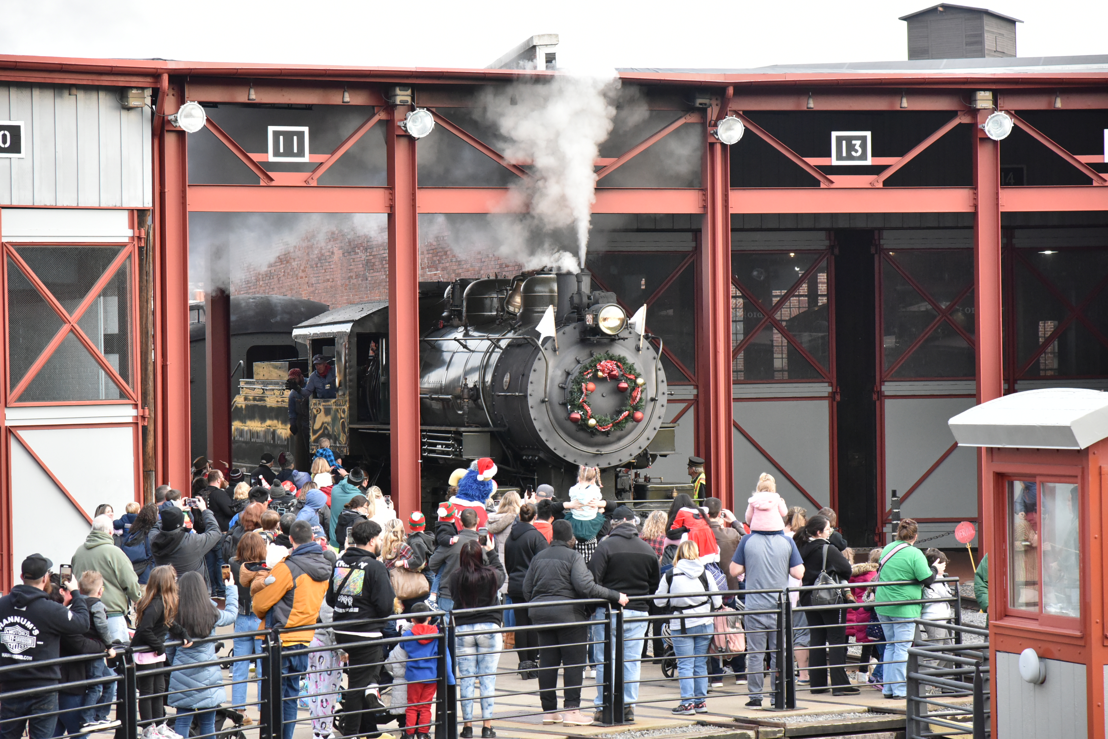 Crowd of visitors gather outdoors as steam engine pulls to turntable