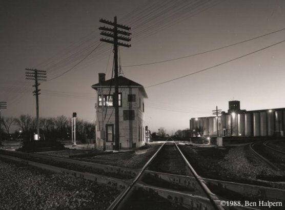 A railroad track diamond - a place where railroad tracks cross each other - withe a switch tower in the background.