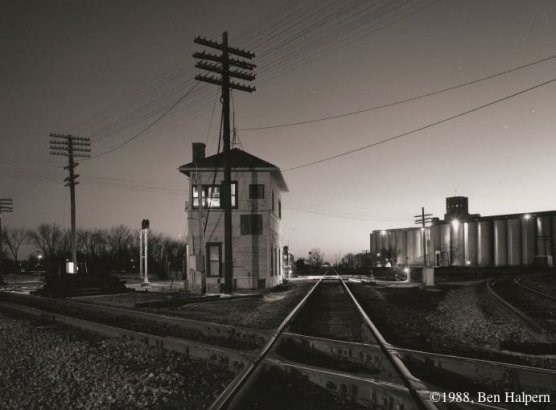A railroad track diamond - a place where railroad tracks cross each other - withe a switch tower in the background.