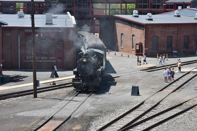 aerial shot of steam locomotive parked in rail yard between buildings