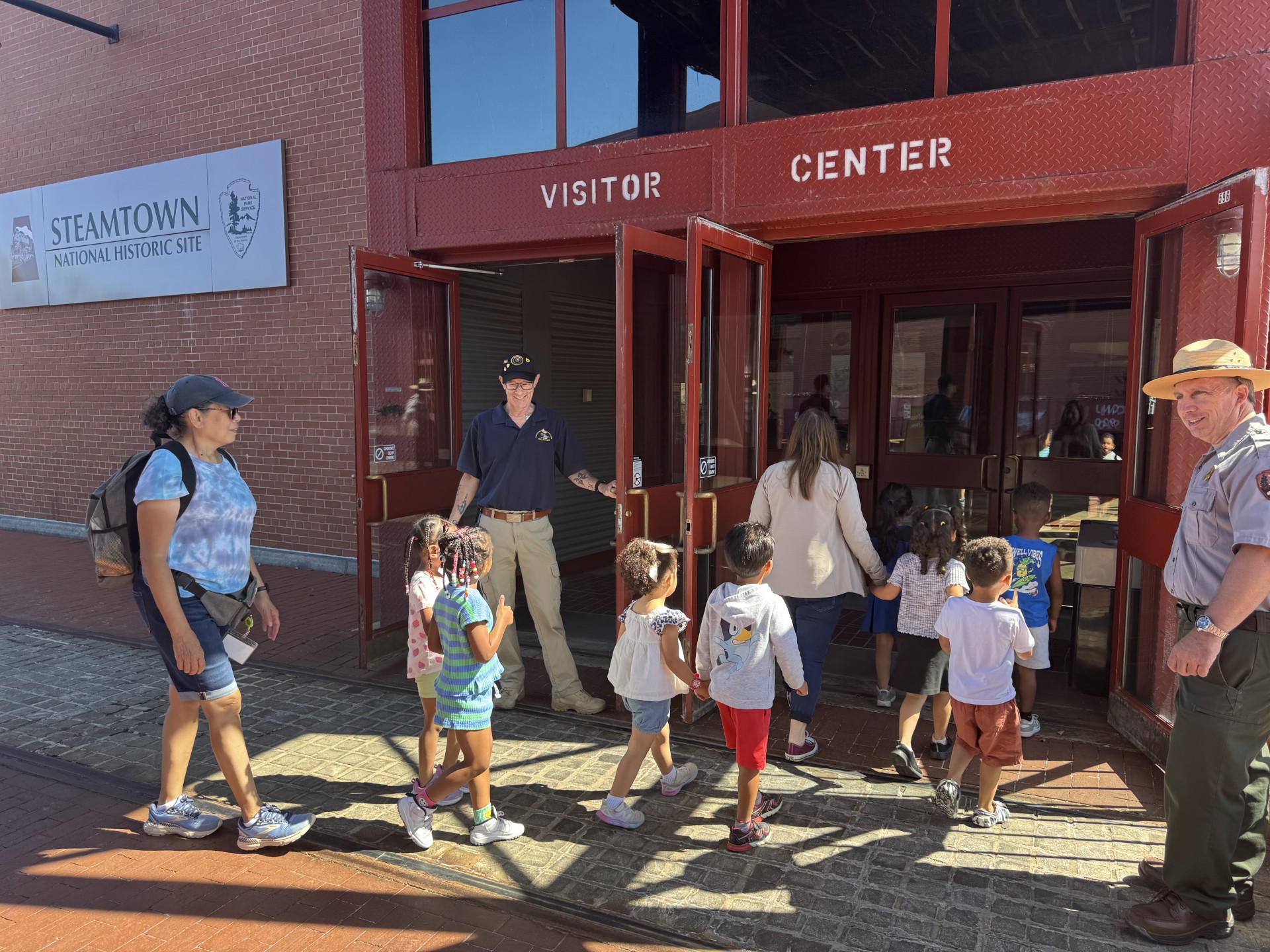 Welcoming visitors inside Steamtown's recently reopened Visitor Center A Steamtown park ranger and volunteer hold the doors open to welcome young learners into the newly reopened visitor center.