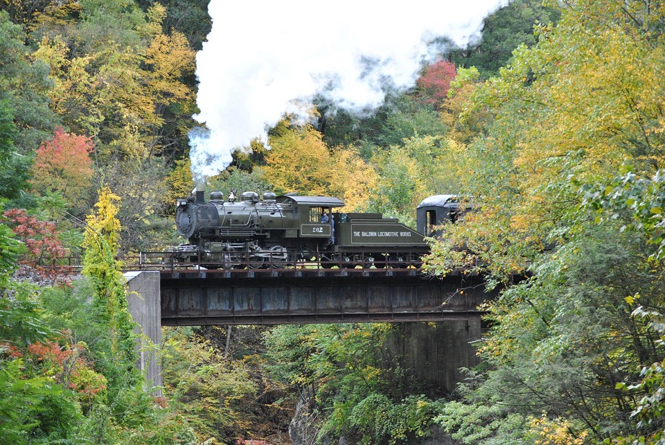 A small steam locomotive crosses a trestle during a fall train ride