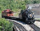 Steam locomotive pulls a flatcar and caboose.