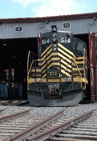 Nickel Plate 514, a dieses-electric locomotive built in 1958, poses half out of the roundhouse doors.  The locomotive is black with yellow stripes.