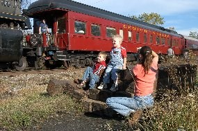 A woman photographs two children with a red passenger car as backgorund. A woman photographs two children with a red passenger car as backgorund.