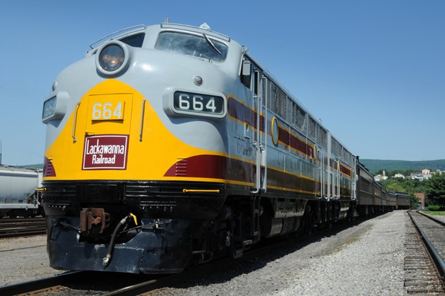 DL&W-painted diesel locomotive, in Lackawanna colors of grey, maroon and yellow, departing Steamtown platform