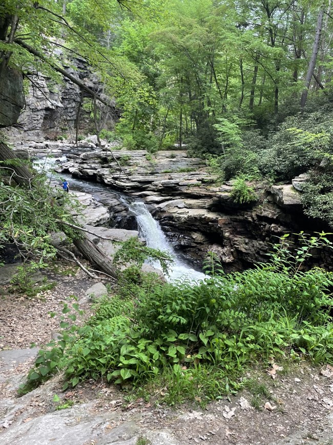 waterfall cascading over shale rocks, trees in the background