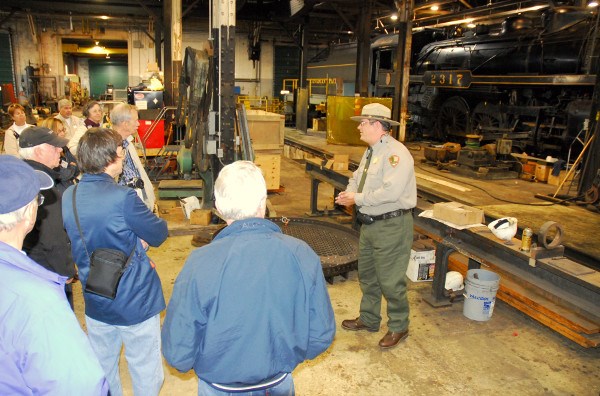 Park Ranger explains locomotive maintenance facilities to visitors on a Locomotive Shop Tour. Park Ranger explains locomotive maintenance facilities to visitors on a Locomotive Shop Tour.