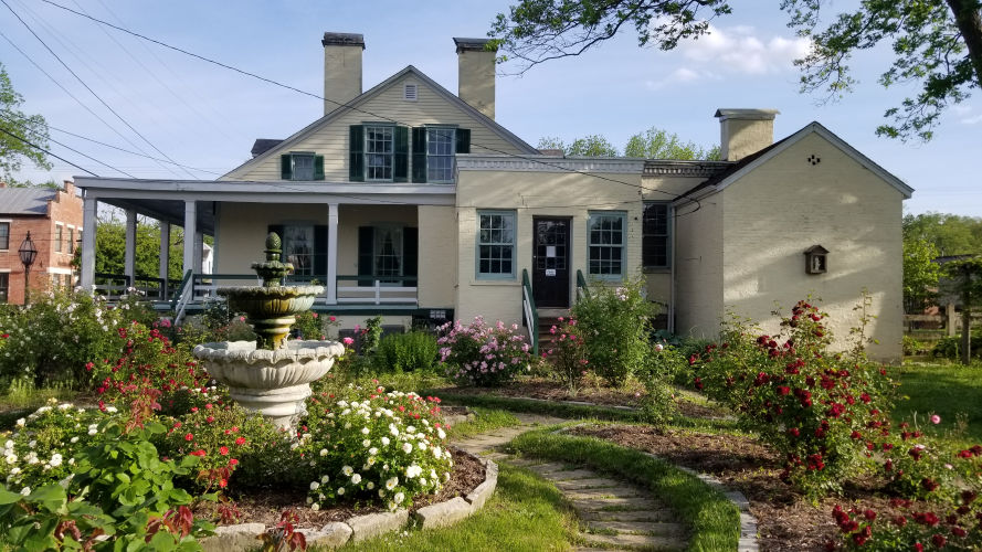 A rose garden in full bloom in front of a historic home