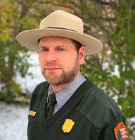 Chris Collins Man in dark green sweater, gray shirt, and wide brimmed hat.