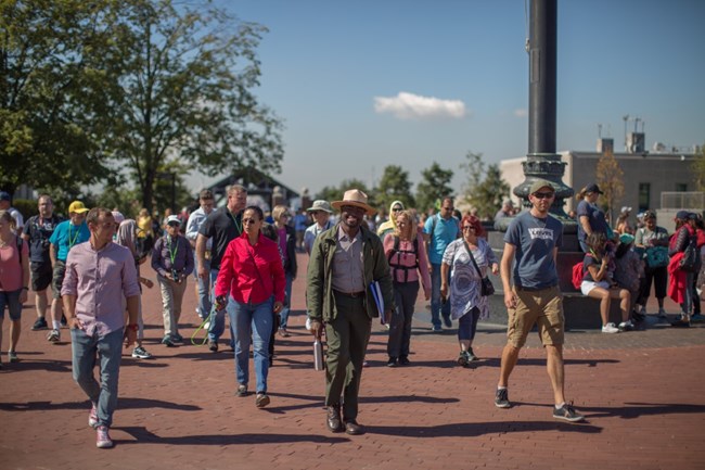 park ranger walking on a sunny day on liberty island with tourists on brick walkway
