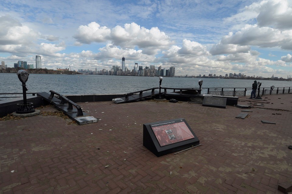 Broken seawall fence and informational tablet laying on a redbrick walkway. Broken seawall fence and informational tablet laying on a redbrick walkway.