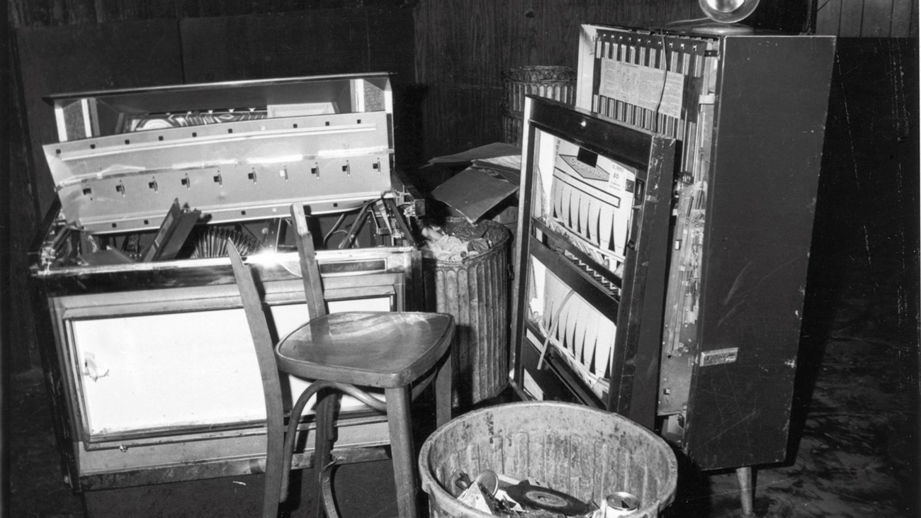 View of a damaged jukebox, cigarette machine, broken chair, and trash can inside of the Stonewall Inn