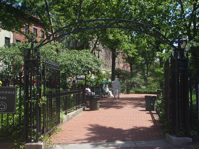 Gated entrance leads to a brick walkway with benches, trees, and several memorials. Gated entrance leads to a brick walkway with benches, trees, and several memorials.