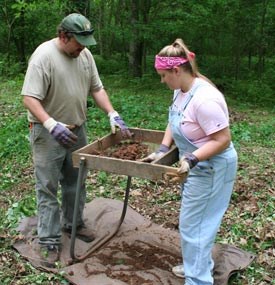 Archeologists sift dirt through a screen.