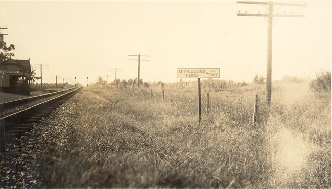 Railroad tracks lie to the right of a stone wall and roofed platform.