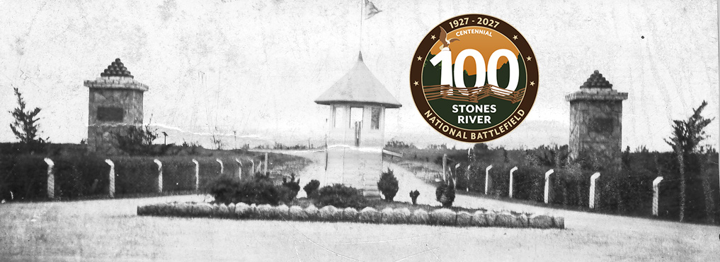 A small building stands in the middle of a road flanked by two stone pillars topped with cannonball pyramids.