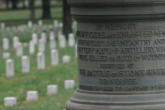 Close-up of a grey stone column with wrap-around writing in a cemetery.