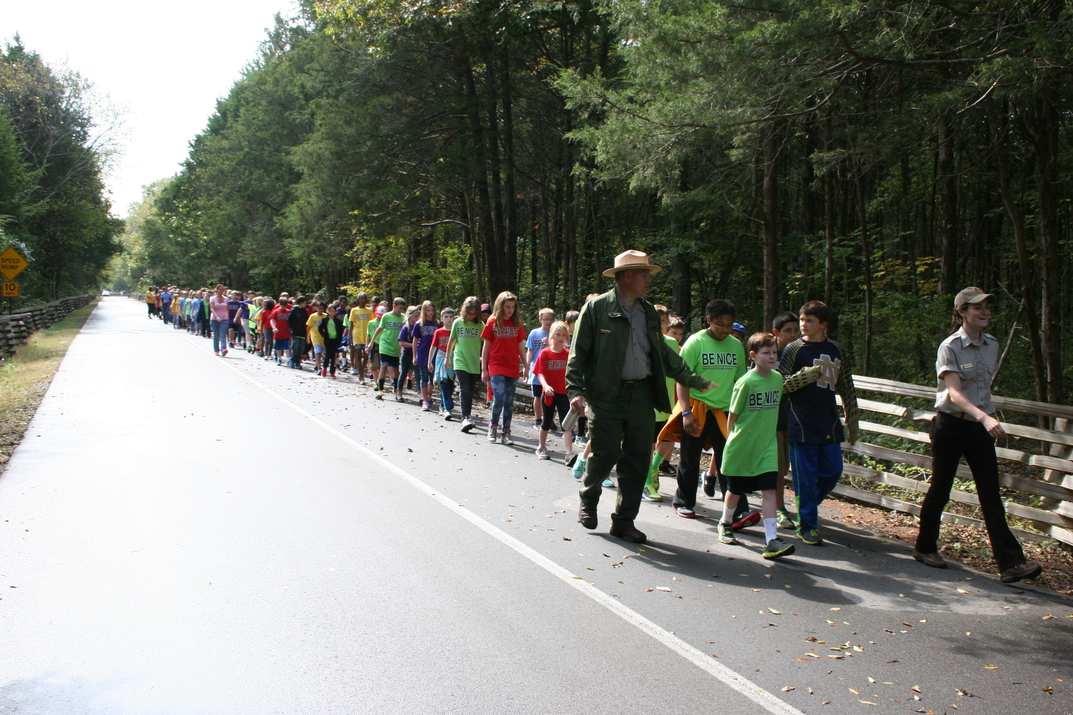 A park ranger leads a group of children walking down a road.