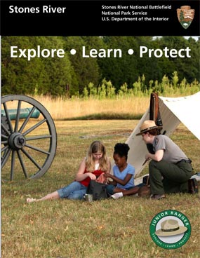 A female park rangers kneels in front of a tent with two seated girls. A cannon is visible in the background.