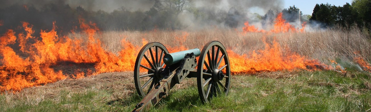 Fire burns in a open field front of a cannon