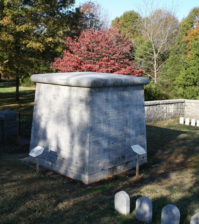 A cube shaped monument and grave markers inside a limestone wall.
