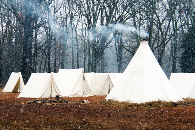 Smoke exits a large white canvas tent with rows of smaller white tents in the background