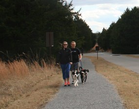 A couple walks their dogs on a gravel trail. A couple walks their dogs on a gravel trail.