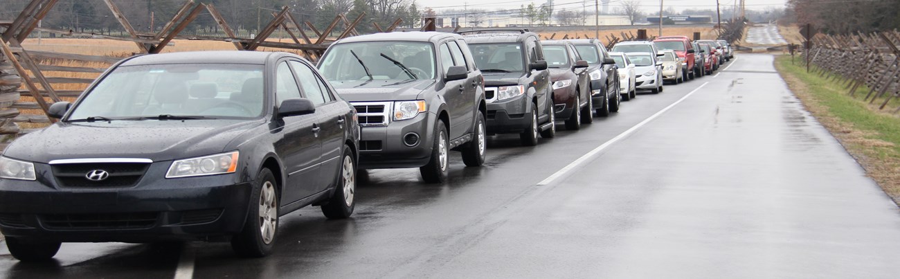 Cars parked in a line on the shoulder of a paved road.