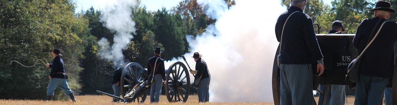 Union soldiers fire a cannon while other soldiers look on.