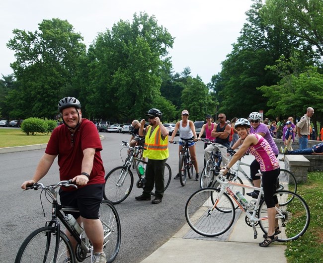 a group of bicyclists stand on their bikes in front of a sidewalk.