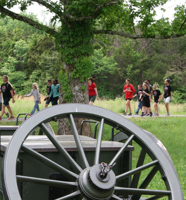 Young people walk on a trail. A green wagon wheel fills the foreground.