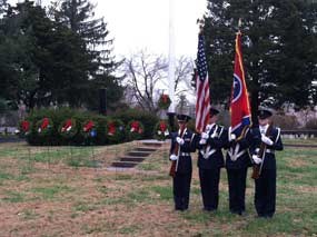 Civil Air Patrol cadets carry flags in front of a row of wreaths.