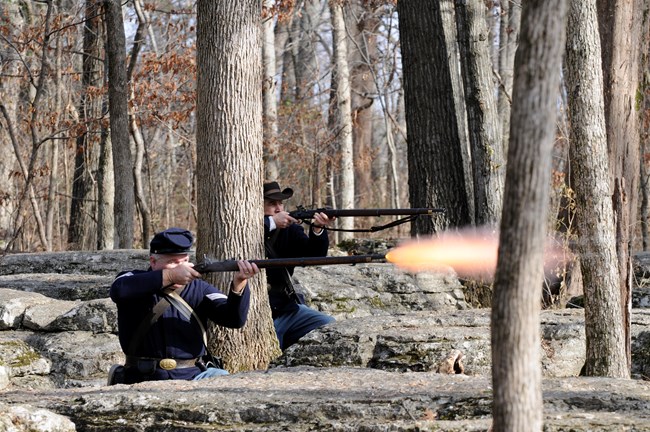 Two Union soldiers fire muskets behind rock outcroppings