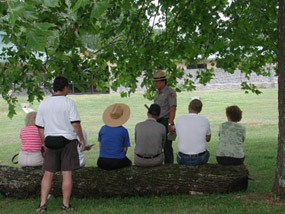 A park ranger talks to visitors sitting on a log. A park ranger talks to visitors sitting on a log.