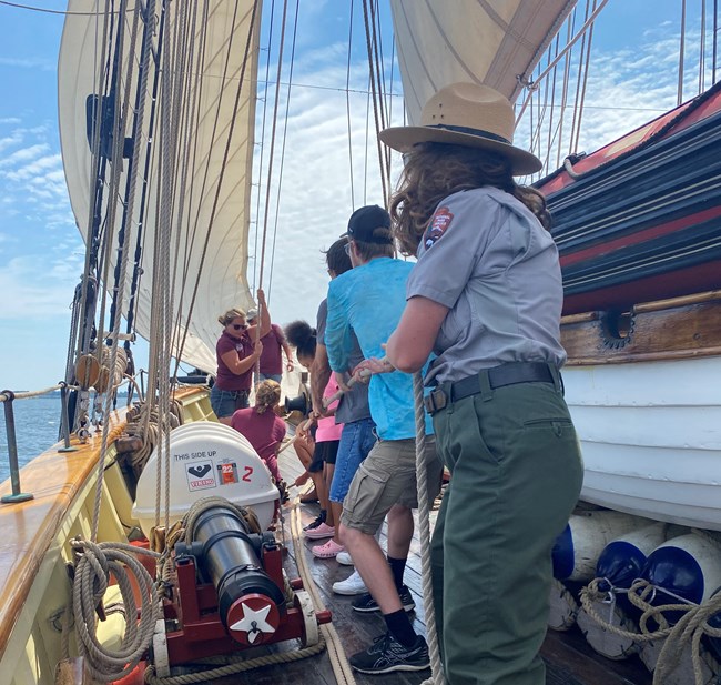 An NPS Ranger helps participants raise a sail onboard the Pride of Baltimore II.