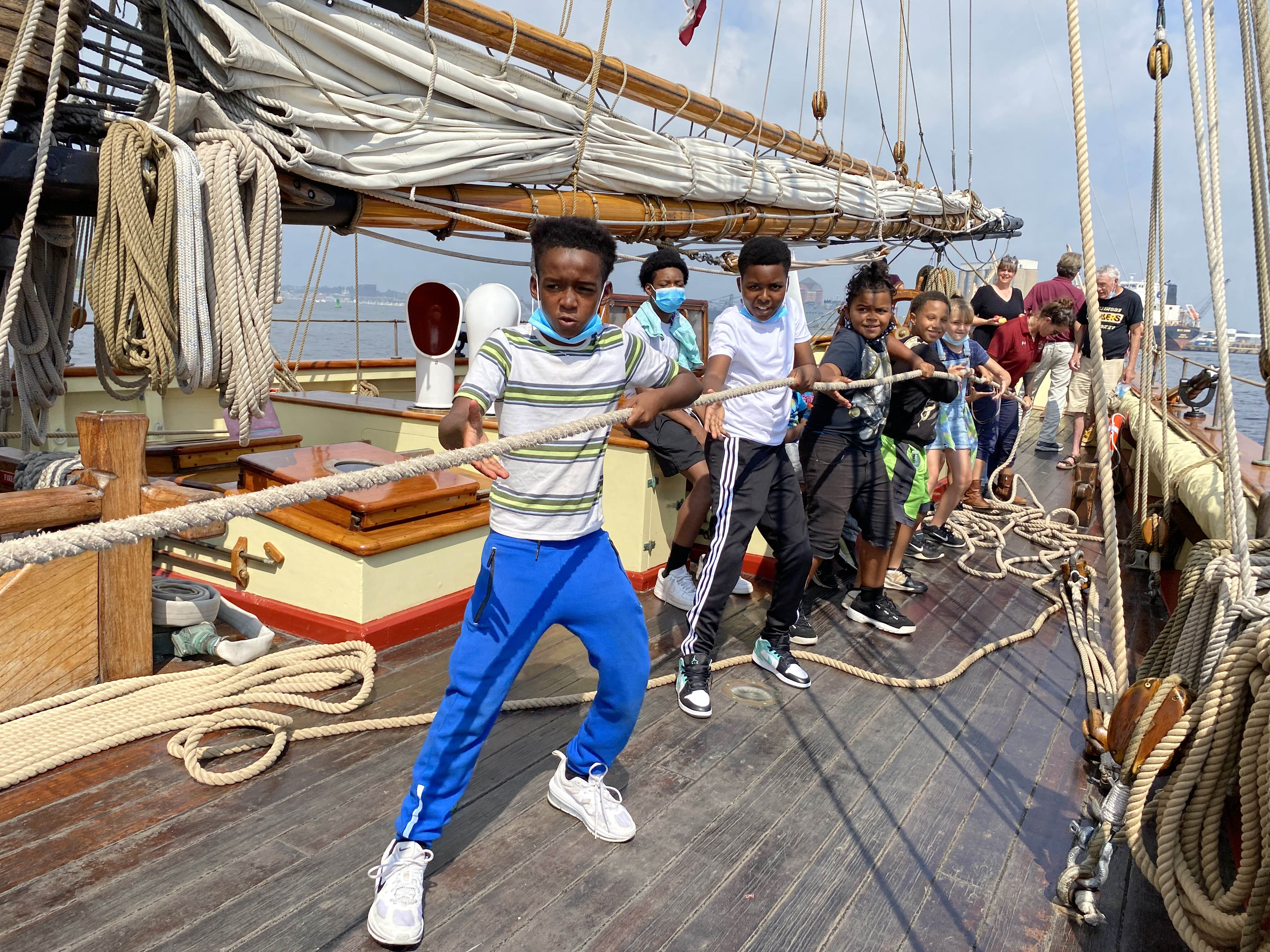 credit: The Tender Bridge A group of students pulls lines on a tall ship.