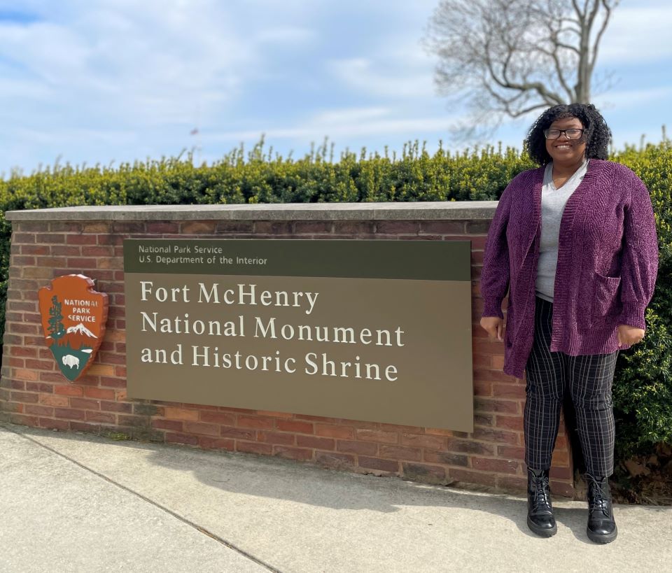 SydniRP_TrailIntern_announcement1-web Young woman standing next to the sign for Fort McHenry
